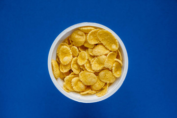 Cornflakes in white bowl on blue background. Top view. Copy, empty space for text