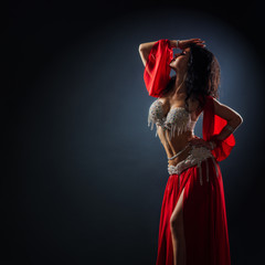 beautiful black-haired girl in red ethnic dress dancing oriental dances in the dark