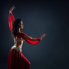 beautiful black-haired girl in red ethnic dress dancing oriental dances in the dark