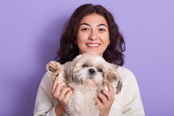 Horizontal shot of positive funny model with peaceful facial expression, raising Maltese paws, spending time with her favourite pet, being fond of animals, having curly black hair. People and pets