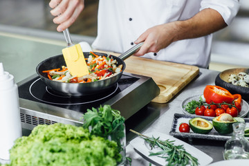 Close up photo, man hands with apron frying vegetables, modern kitchen. Vegan and healthy life concept.