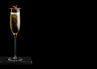 Elegant glass of yellow champagne with rasspbery on stick on black marble board on black background. Space for text