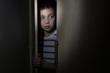 Scared little boy hiding in wardrobe. Domestic violence concept