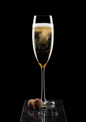 Elegant glass of yellow champagne with cork and wire cage on black marble board on black background.