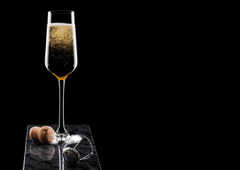 Elegant glass of yellow champagne with cork and wire cage on black marble board on black background. Space for text