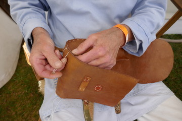Saddler. Leather craftsman at work. He  sews a bag by hand. Close-up. - obrazy, fototapety, plakaty