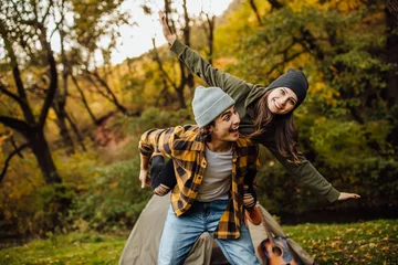 Tuinposter Happy loving couple of tourist have fun and make airplane. Happy young man piggybacking his girlfriend while keeping arms outstretched. © Тарас Нагирняк