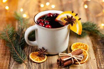Christmas hot mulled red wine in white mug with spices and fruits on a wooden rustic table. Traditional warming winter drink for holiday time. Cozy home atmosphere