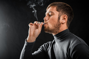 A man Smoking a cigarette rolled dollar in a tube, the concept of addiction, addiction and waste of money and money