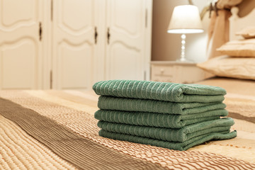 Stack of green hotel towel on bed in bedroom interior