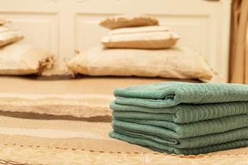 Fototapeta na wymiar Stack of green hotel towel on bed in bedroom interior