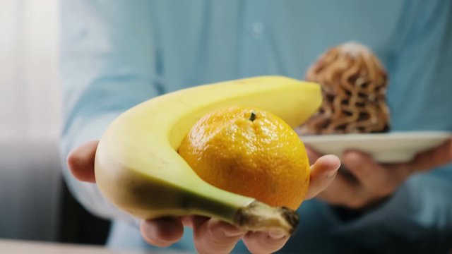 A man shows fruit and a cake in his hands. Choosing a healthy diet and fruit diet. slimming and healthy eating concept