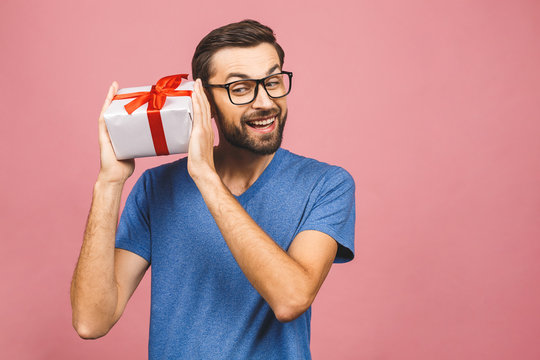Wonderful gift! Adorable photo of attractive man with beautiful smile holding his birthday present box isolated over pink background.