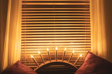 A modern advent candlestick in a window with the blinds down that forms a striped pattern