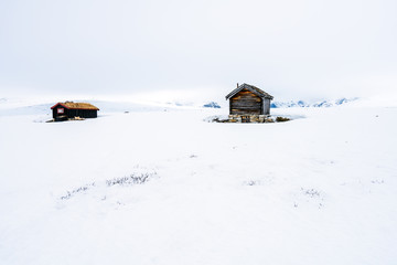 A old and ancient wooden cabin outdoors in beautiful snow covered mountains and foggy scenery with cross coutry skiiers in the background. Architecture and season concept. 