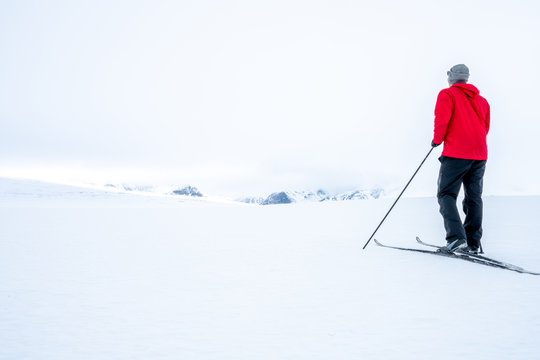 Man in red jacket doing cross country skiing during foggy weather in the mountains of Norway, looking towards the beautiful mountain scenery landscape. Freedom, sports, active and outdoors concept.