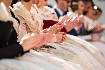 Falleras seated clapping at a public event in the city. Group of unfocused falleras.