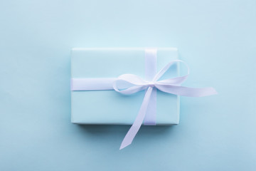 gift in a blue box tied with a white ribbon on a blue background top view