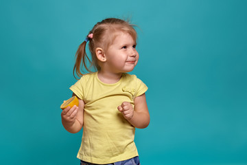 Close-up studio shot of a beautiful little girl. Little blonde girl in a yellow t-shirt on a blue background. The emotions of a child who eats a lemon.