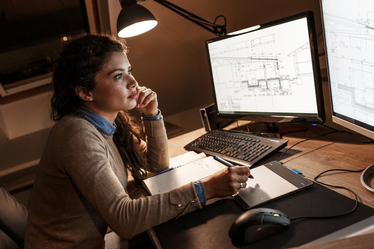 Female engineer working at home. She's using a digital pen and examining the blueprint on screen.	