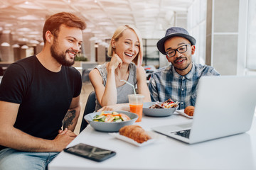 Happy coworkers using laptop during lunch