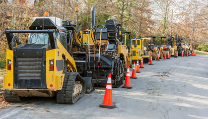 Long line of asphalt pavers and rollers parked on neighborhood street.