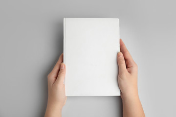 Woman holding book with blank cover on grey background, top view