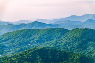 Layers of mountains in the haze during sunset. Beautiful sunset in the mountains. Beautiful sunset in a hilly valley with villages and fog in the lowlands.