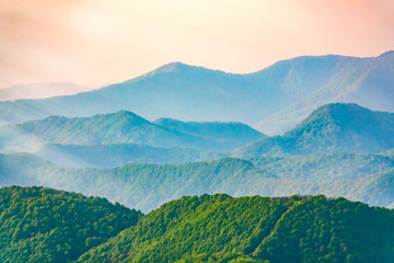 Layers of mountains in the haze during sunset. Beautiful sunset in the mountains. Beautiful sunset in a hilly valley with villages and fog in the lowlands.