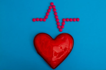 Red heart and an electrocardiogram graph of pink tablets on a blue background. Pharmaceutical...