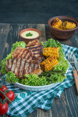 Grilled steak in a round bowl with spices, herbs and vegetables on a dark wooden background. Space for text.