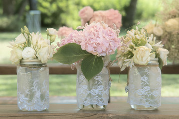 Bouquet of hydrangeas and roses flowers on wooden table close up in a glass pots in open air. Shabby chic 
