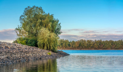 Green willow on the river bank. Paradise Beautiful nature. Clear blue sky and turquoise water. Trees are reflected in the water. Travel and vacation. © Valentin Kundeus