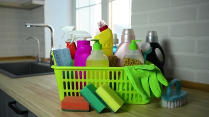 household chemicals in basket on kitchen background
