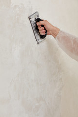 Hand of a man sanding a wall after plastering