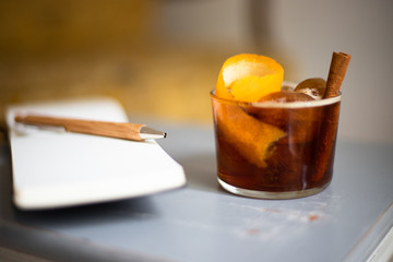 Cold brew coffee drink with orange peel and cinnamon stick arranged with pen and a notepad on a...