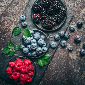 Fresh berries with raspberries, blueberries, blackberries in bowl on a stone stand on a dark metal background.