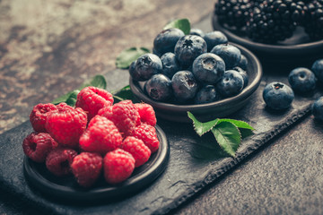 Fresh berries with raspberries, blueberries, blackberries in bowl on a stone stand on a dark metal background.