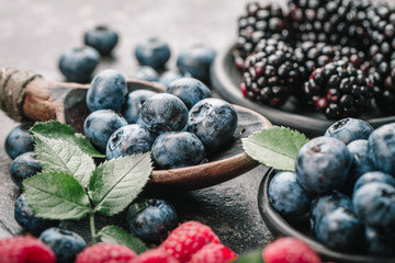 Fresh berries with raspberries, blueberries, blackberries in bowl on a stone stand on a dark metal background.