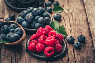 Fresh berries with raspberries, blueberries, blackberries in bowl on a stone stand on wood background.