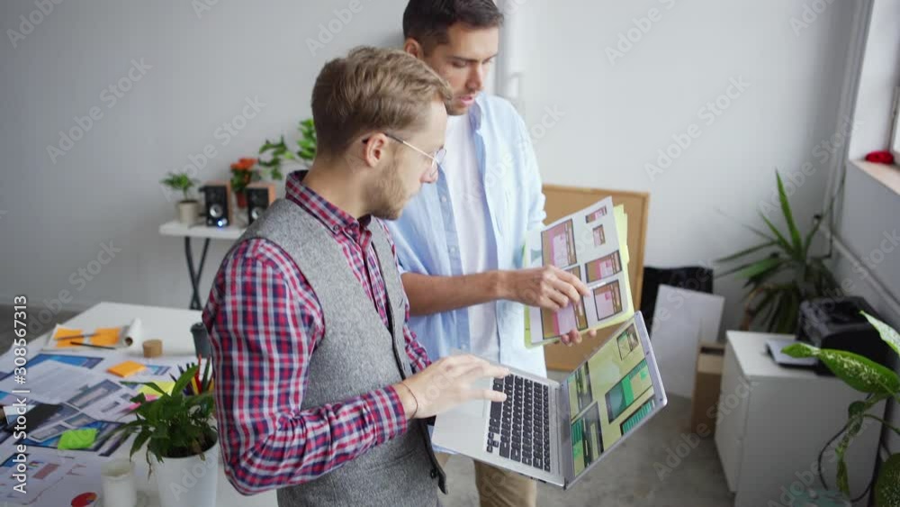Wall mural tilt up of two young creative web designers standing in office and discussing application interface 