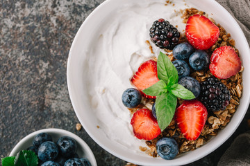 Healthy breakfast with granola, yogurt, fruits, berries on dark metal background. Summer homemade breakfast.