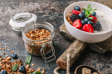 Healthy breakfast with granola, yogurt, fruits, berries on dark metal background. Summer homemade breakfast.