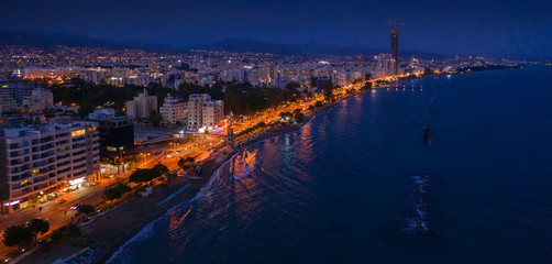 Fototapeta premium Aerial view of Limassol promenade or embankment with alley and buildings in Cyprus at night. Drone photo of mediterranean sea resort Limassol from above.