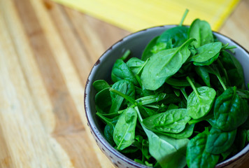 Fresh spinach leaves in a bowl on a wooden table. Eco vegan spinach salad