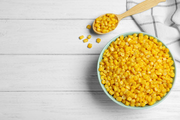 Delicious canned corn in bowl on white wooden table, flat lay. Space for text