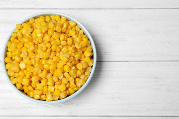 Delicious canned corn in bowl on white wooden table, top view. Space for text