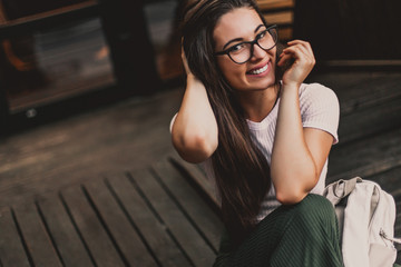 Happy smiling woman in glasses sitting on wooden steps in street.