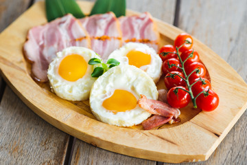 Tasty fried eggs with vegetables on a wooden plate.