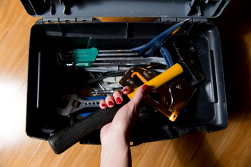 female hand with red manicure pulls a hammer from a tool box